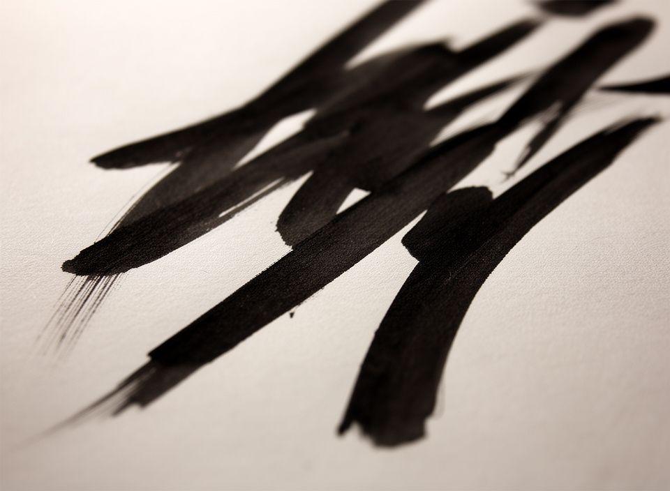 Kalligraphische Pinselstriche auf Papier mit tiefschwarzer Tinte und weicher Lichtkante